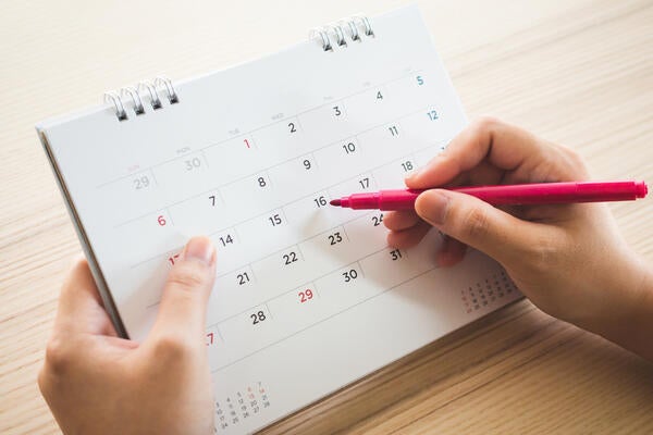 A person writing on a calendar with a pen